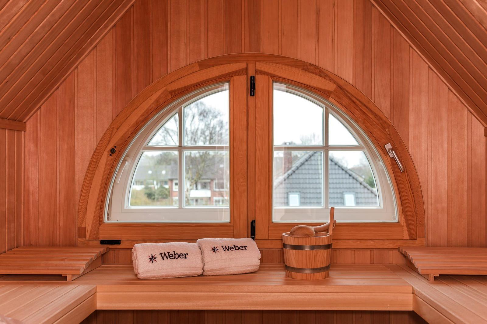Holzsauna mit Badekorb und Fenster. Handtücher mit Logo liegen bereit.