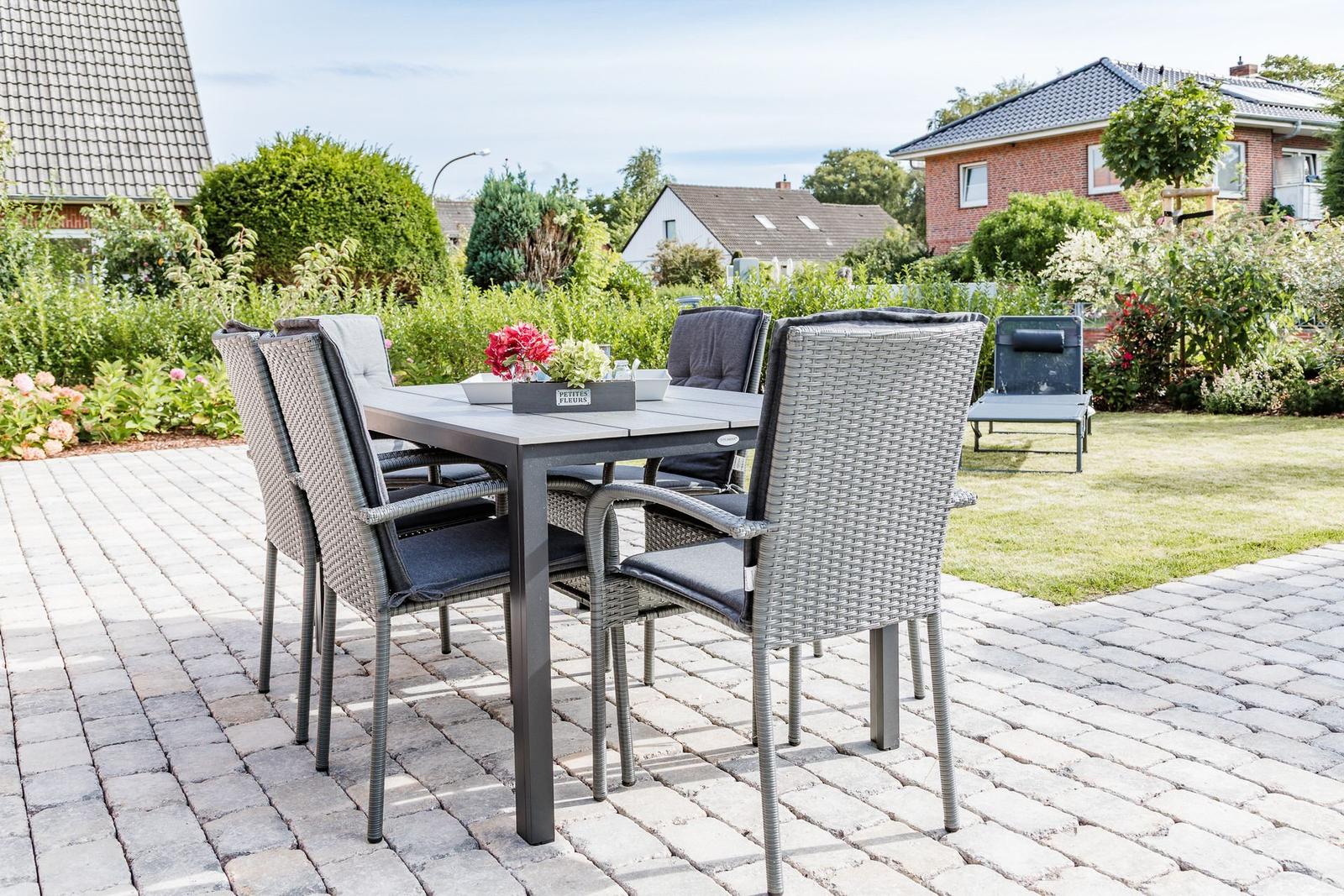 Garten mit Tisch und Stühlen auf gepflastertem Platz. Hintergrund mit Grünflächen und Häusern.