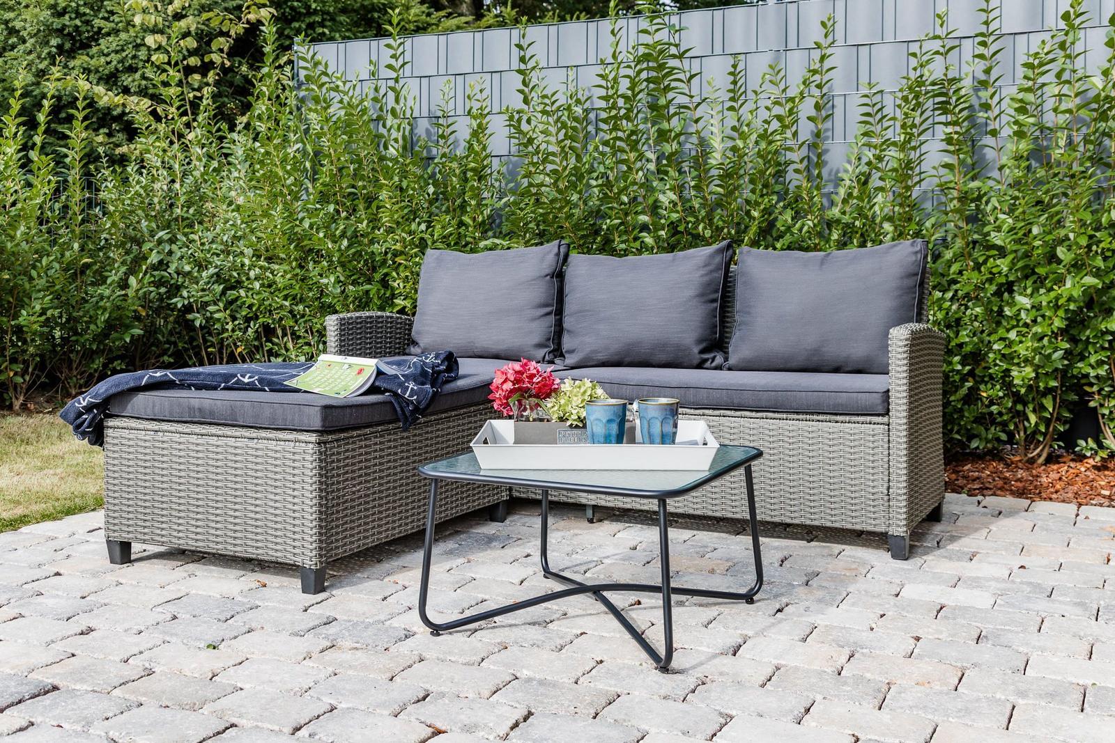 Garten mit grauem Rattan-Sofa und Tisch mit Blumen.