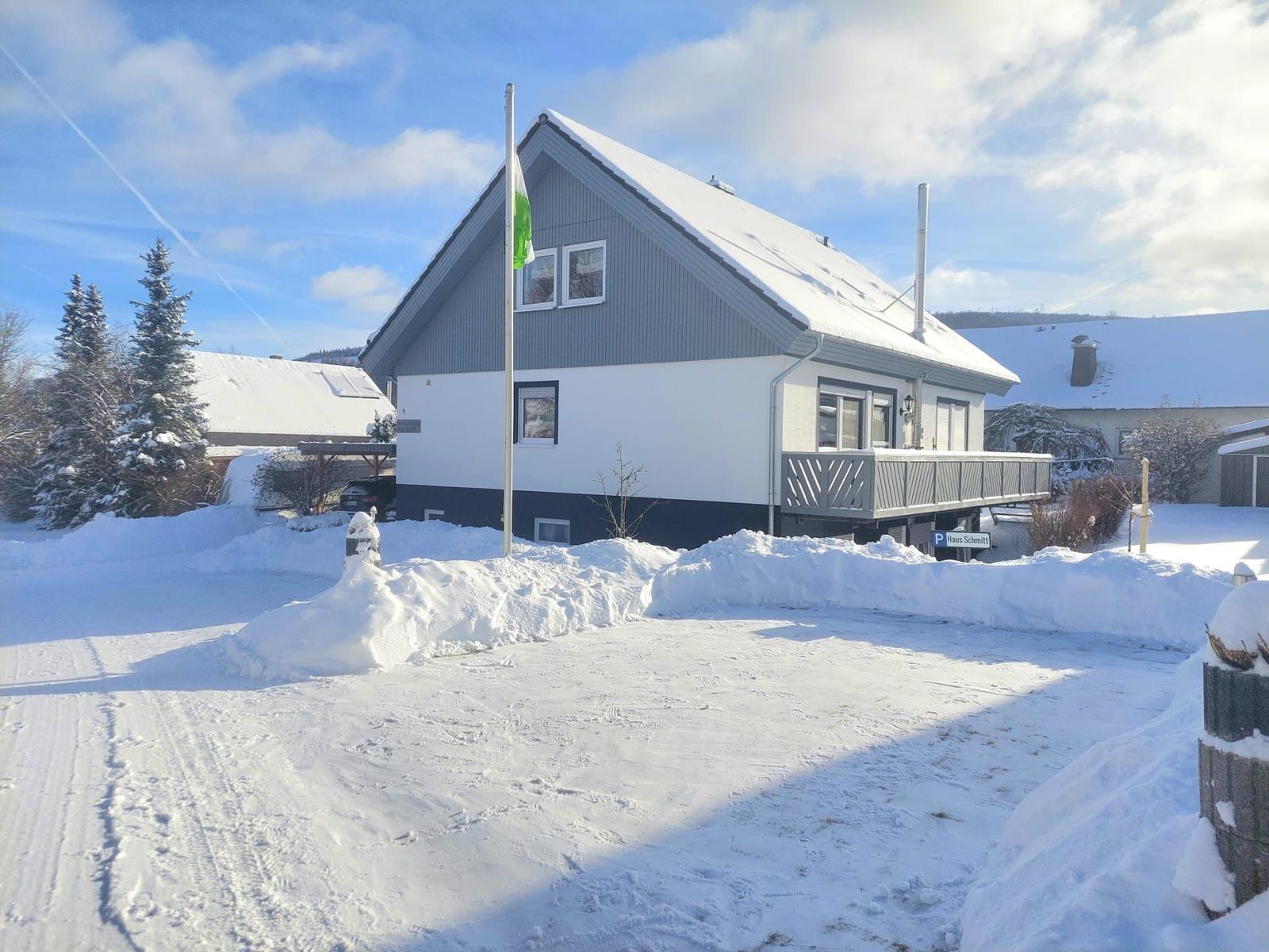 Schneebedecktes Haus mit Balkon und Fahnenmast im Winter.