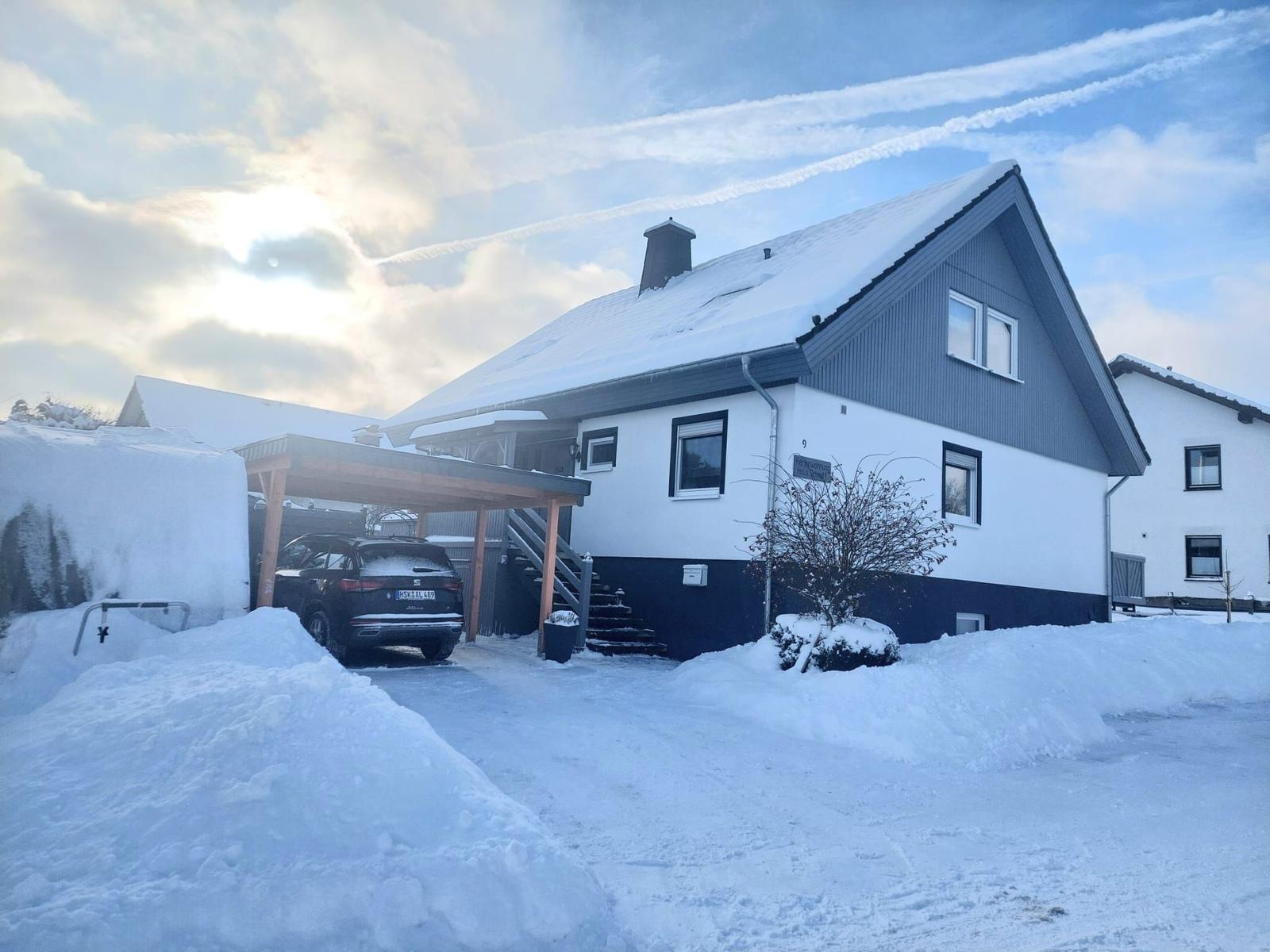 Wohnhaus mit Schneebedecktem Dach und Carport. Ein Auto steht unter dem Carport.