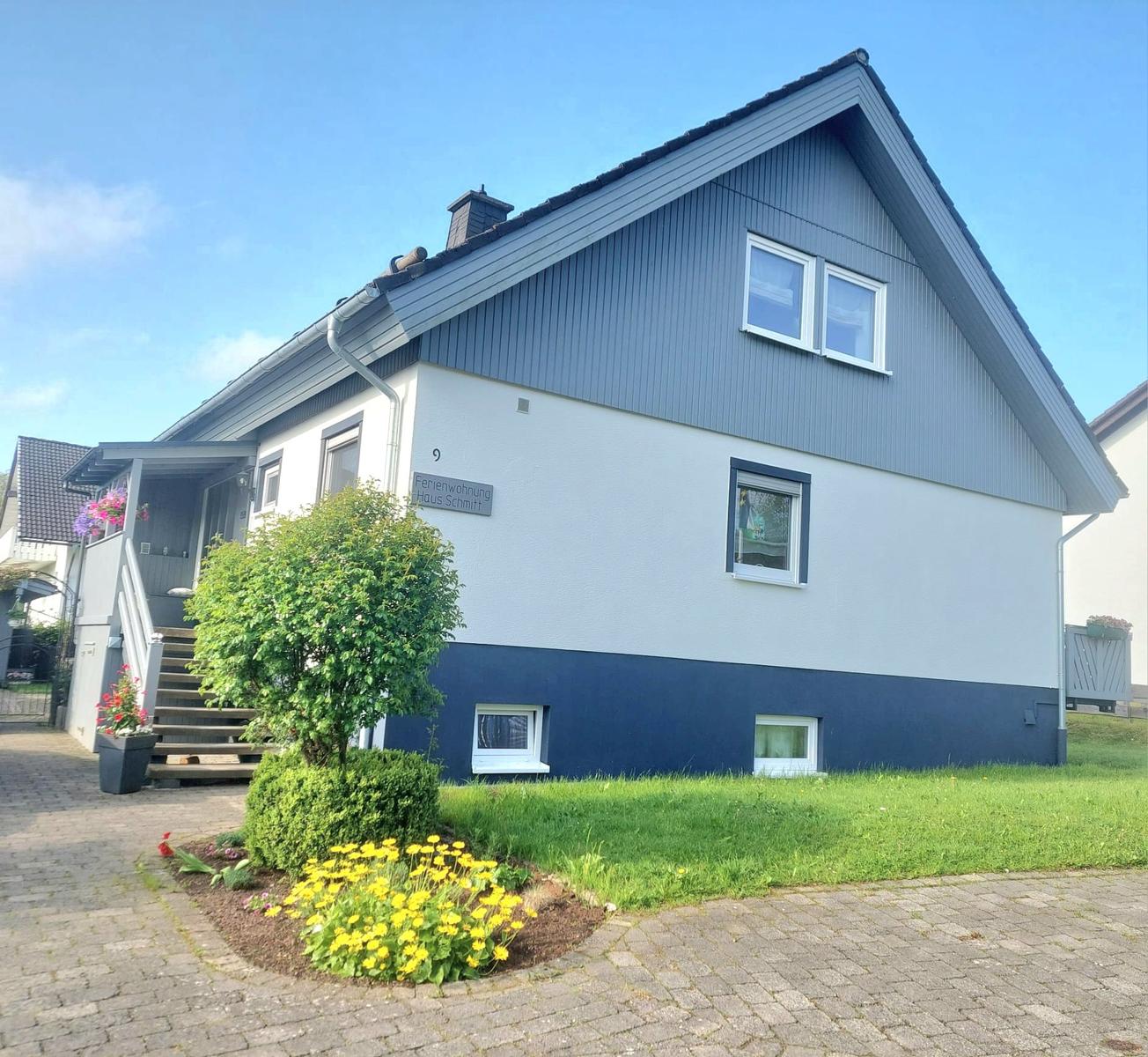Ferienhaus mit blau-weißer Fassade, Vorgarten mit Blumen und Treppenhaus.