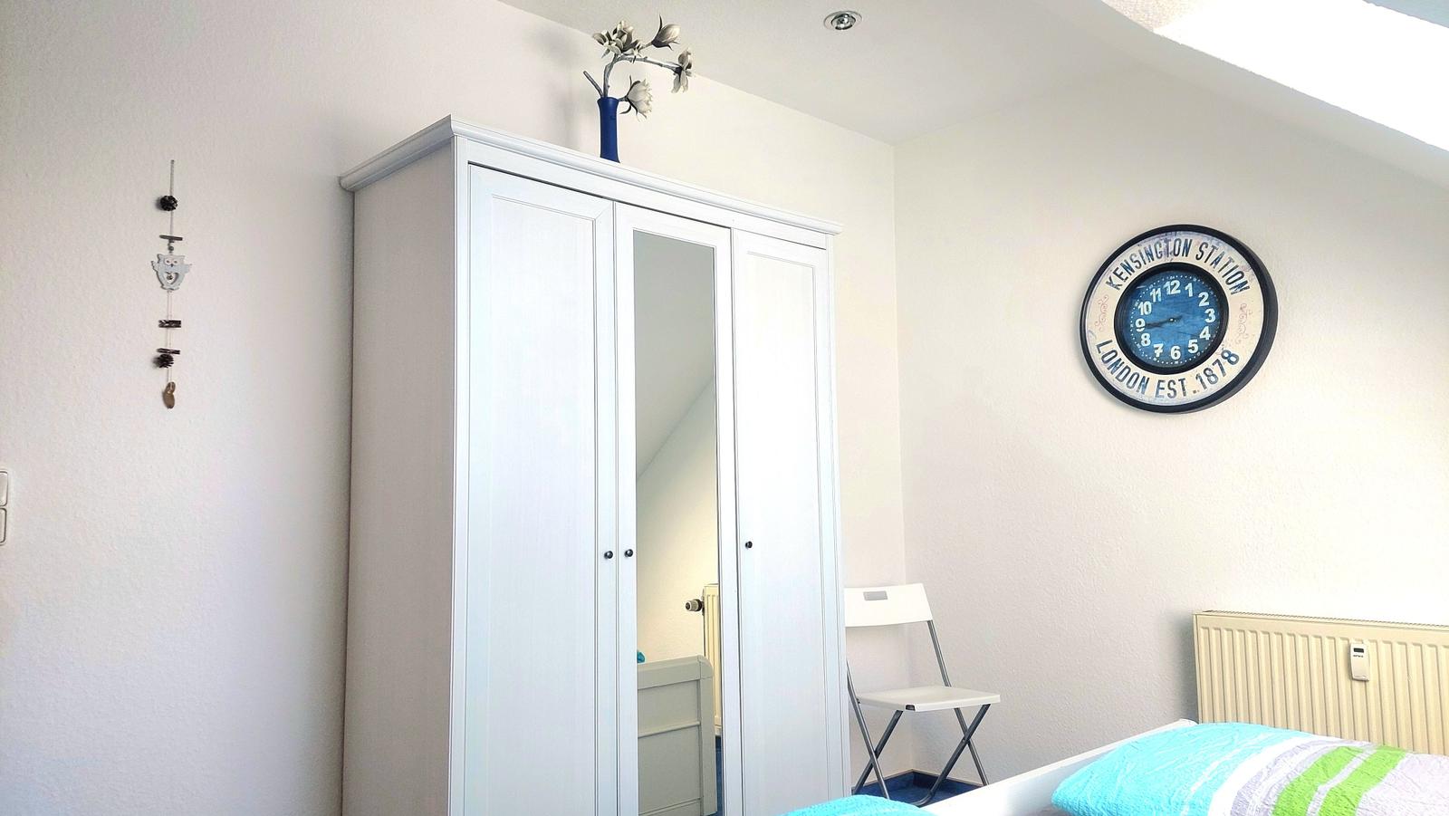 Schlafzimmer mit Kleiderschrank, Wanduhr und Bett