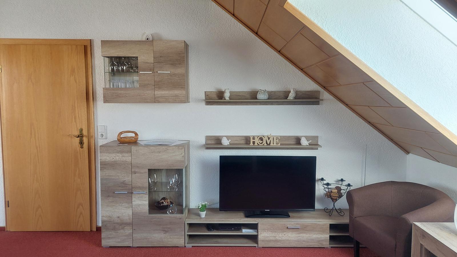 Wohnzimmer mit TV, Schränken und Sitzgelegenheit unter Dachschrägen.