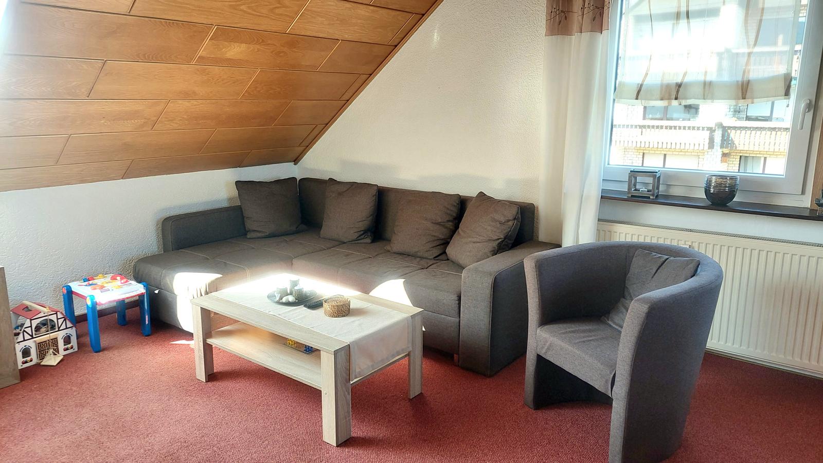 Wohnzimmer mit Sofa, Sessel und Holzdecke.