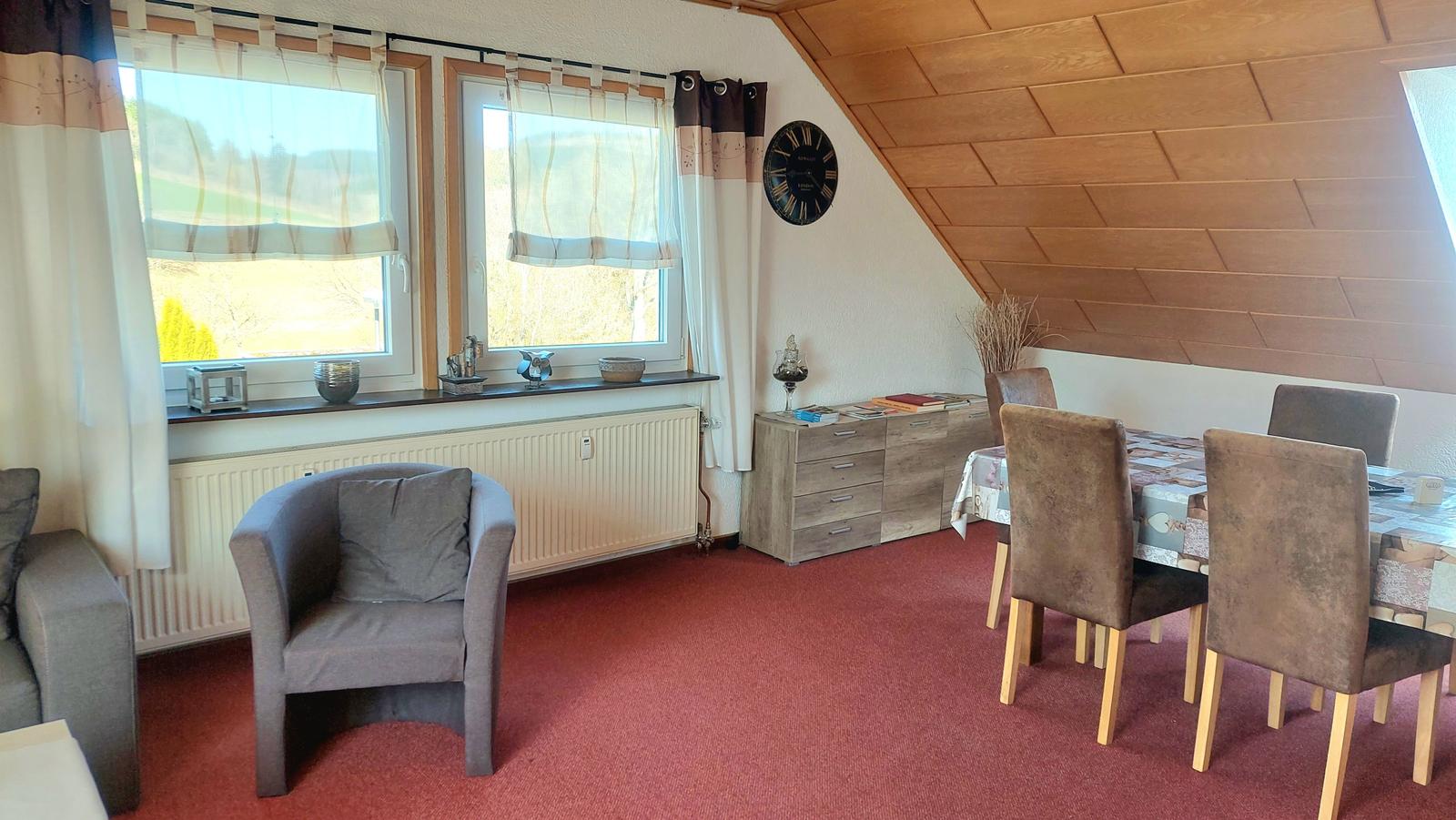 Wohn- und Essbereich mit Tisch, Stühlen, Fenstern und Holzdecke.