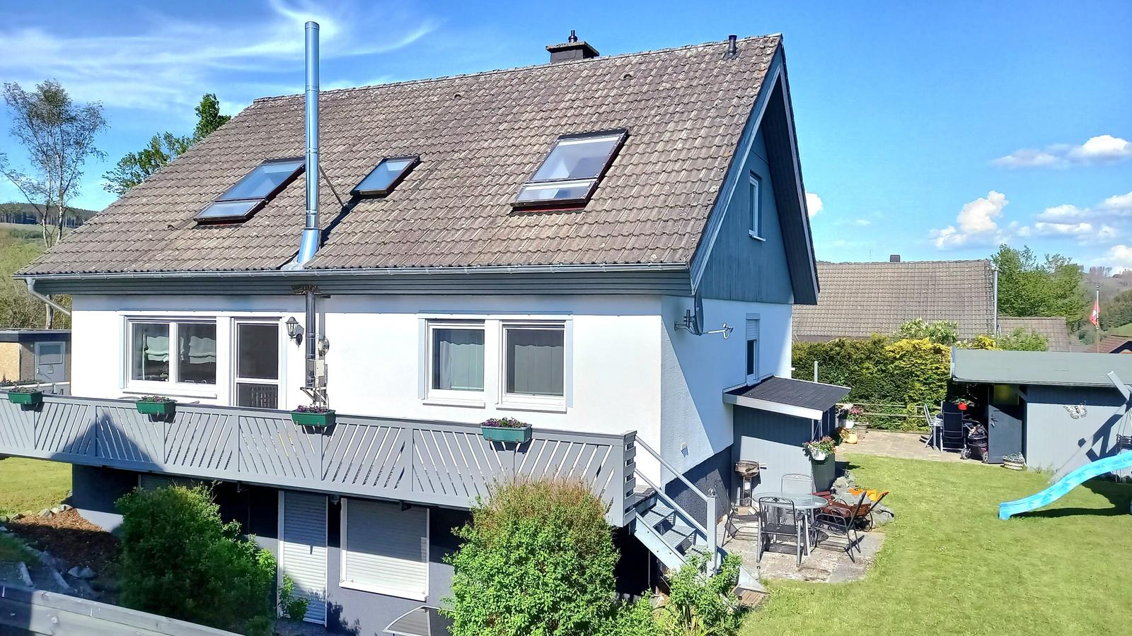 Haus mit Balkon, Garten und Dachfenstern. Außenterrasse mit Gartenmöbeln.