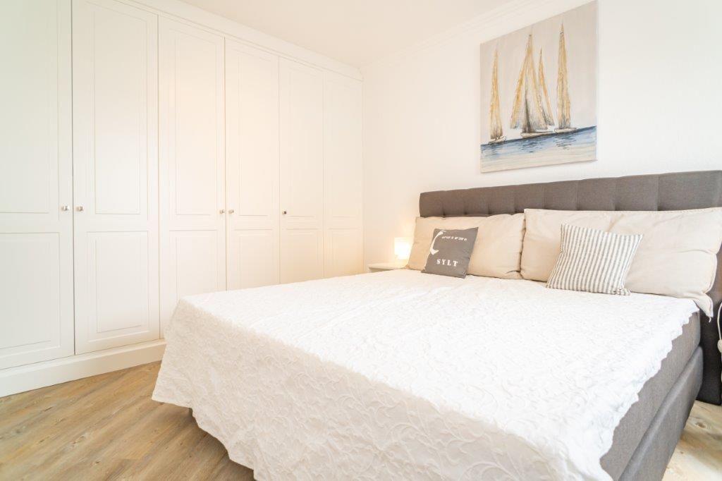 Schlafzimmer mit großem Bett, weißen Schränken und Segelyacht-Bild an der Wand.