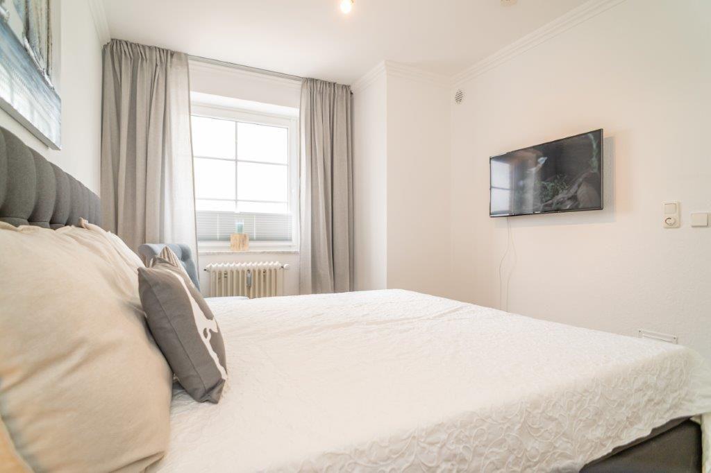 Schlafzimmer mit Bett, Fenster und Wandfernseher.