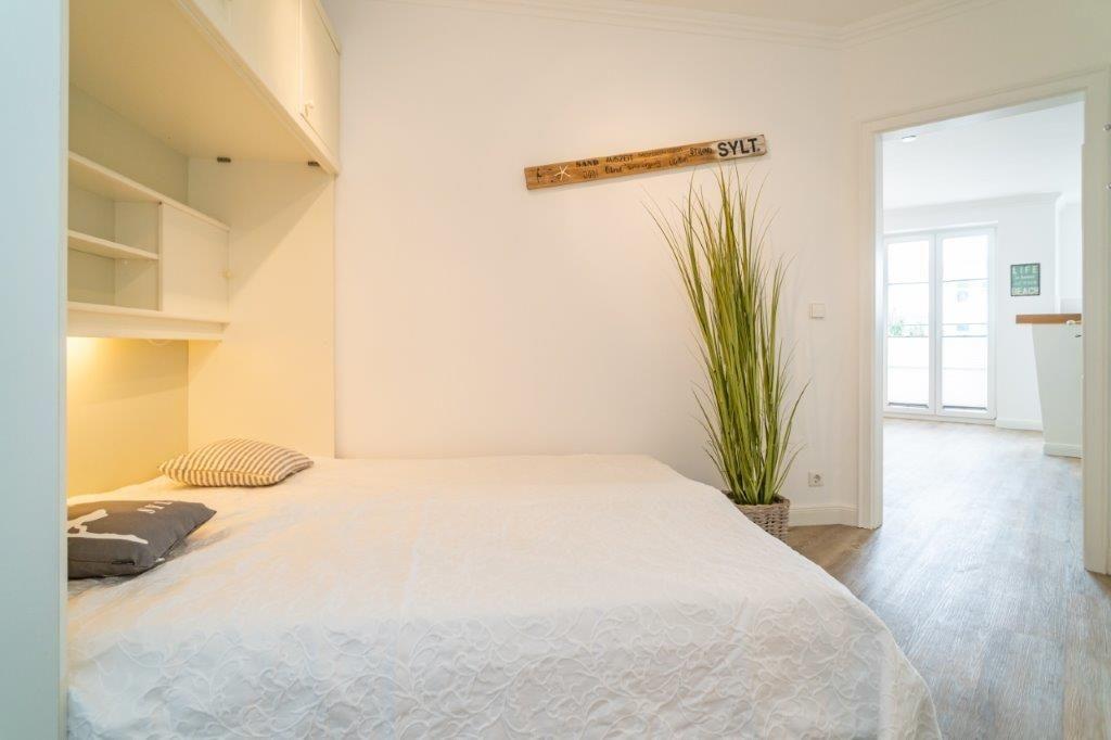 Schlafzimmer mit Bett, Regal und Pflanze. Sicht auf Wohnbereich.