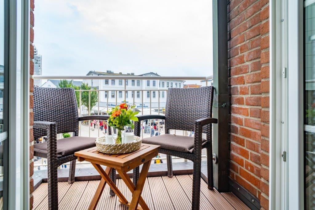 Terrasse mit zwei Stühlen, Tisch und Blumenstrauß. Blick auf Gebäude und Straße.