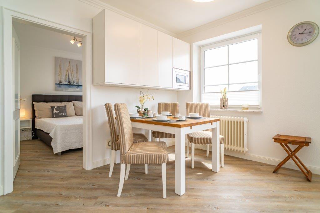 Essbereich mit Tisch und Stühlen, Küchenzeile und Blick in Schlafzimmer.