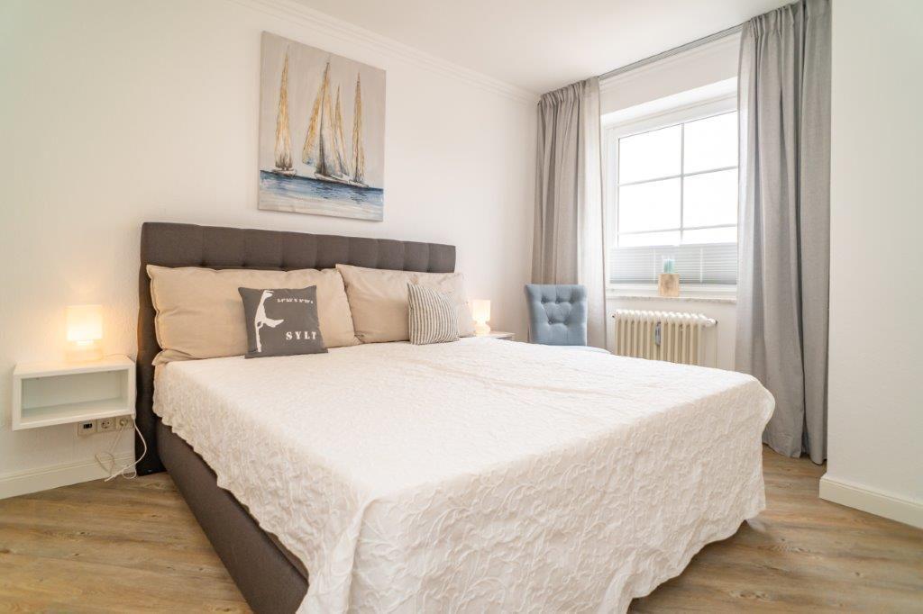 Schlafzimmer mit Bett, Wandbild und Fenster mit Vorhängen.