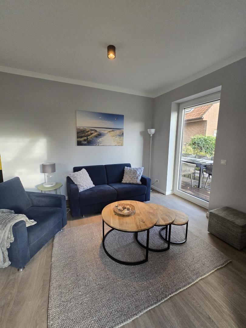 Wohnzimmer mit Sofa, Sessel und runden Tischen. Durchgang zur Terrasse.