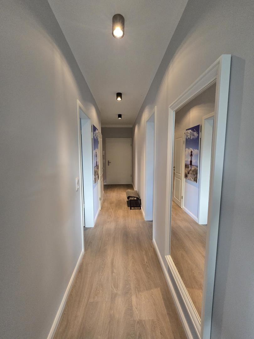 Flur mit Holzboden und Türen zu Räumen, Wandbilder und Deckenleuchten.