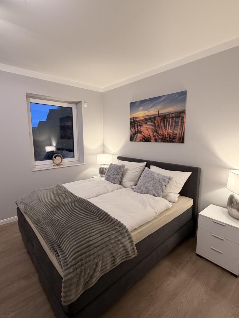 Schlafzimmer mit Doppelbett, Fenster und Wandbild.