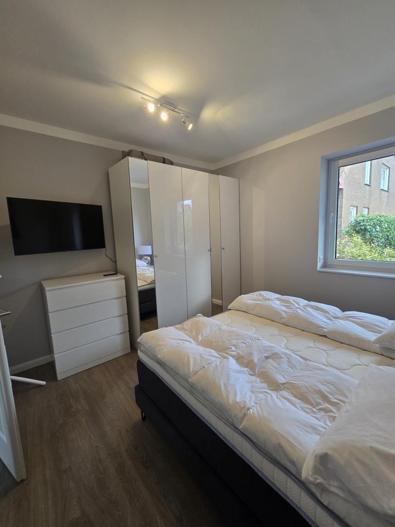 Schlafzimmer mit Doppelbett, Schrank und TV. Fenster mit Blick auf Grün.