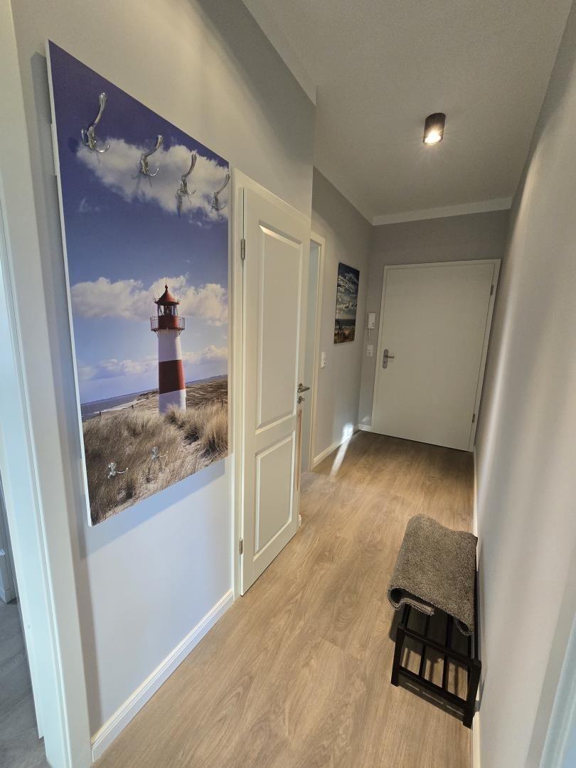 Flur mit Holzboden, Wandbild Leuchtturm und Haken. Tür zu Wohnraum und Bad.