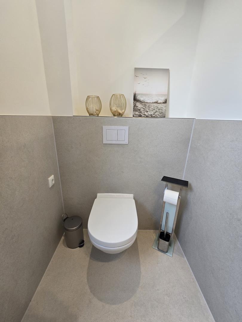 Toilette mit Wandhalterung, Toilettenbürste und dekorativen Objekten.