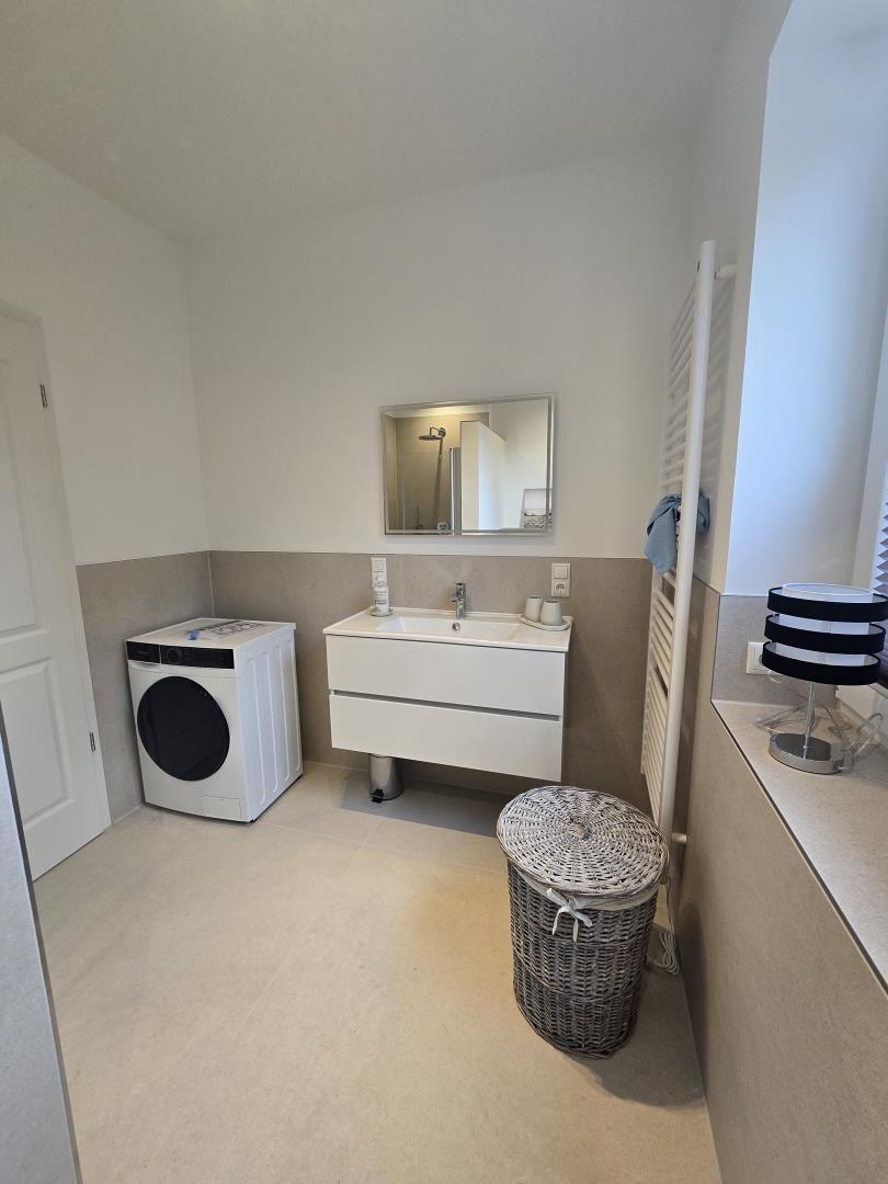 Badezimmer mit Waschmaschine, Waschtisch und Spiegel.