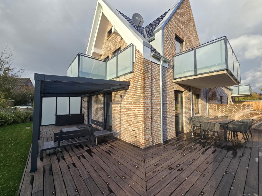 Haus mit Holzterrasse, Glasbalcony und Außensitzgelegenheiten.