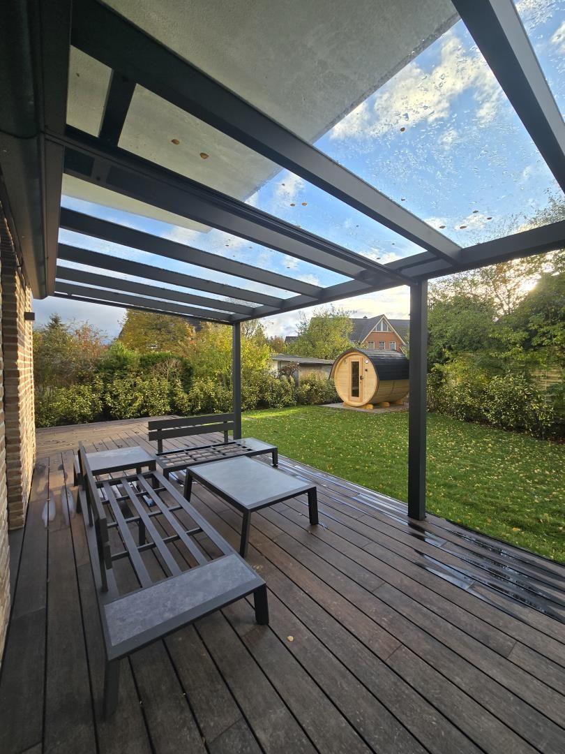 Terrasse mit Holzdecke, Sitzgelegenheiten und Garten mit Sauna.