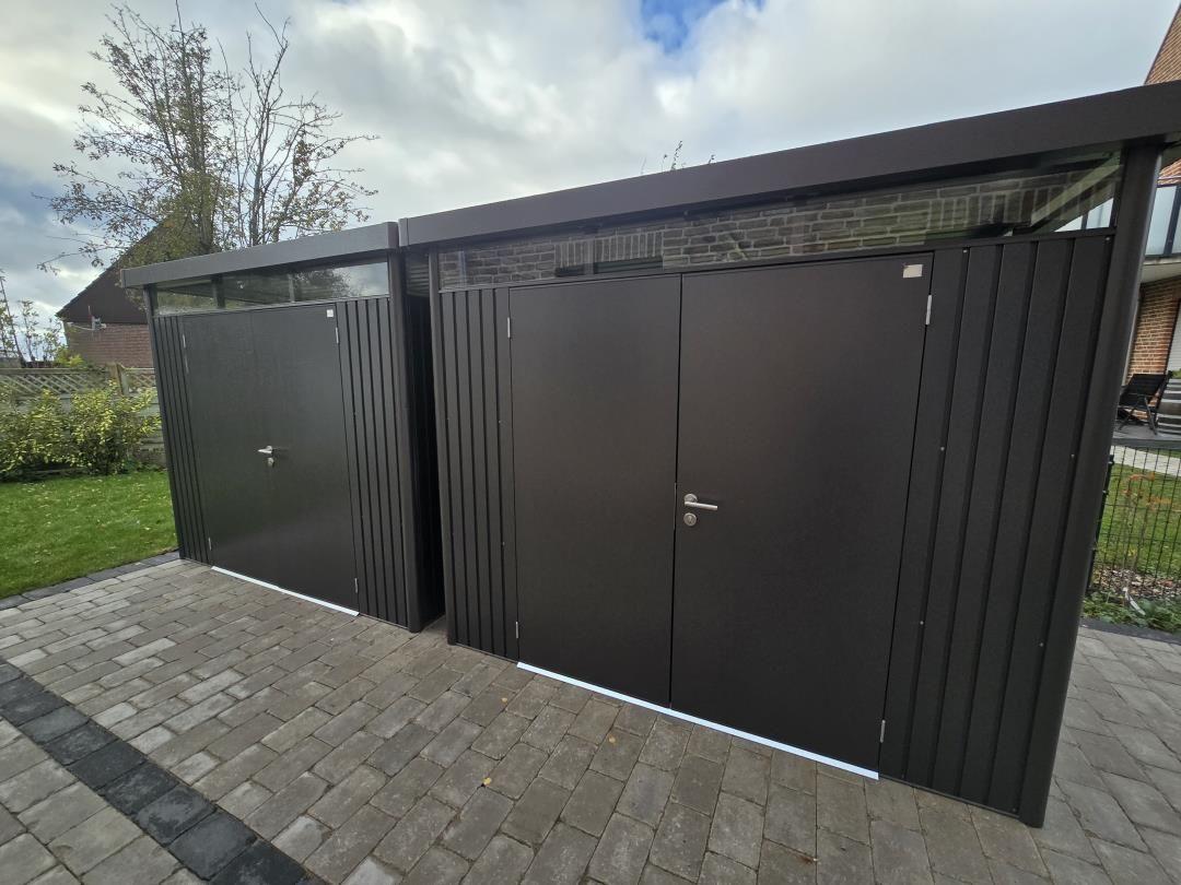 Zwei dunkle Metallgaragen mit Türen auf gepflastertem Grundstück.