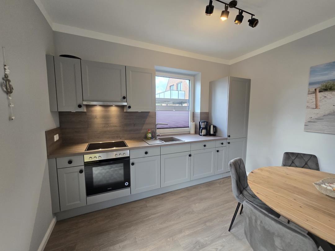 Küche mit Essbereich, graue Schränke, Holztisch und Fenster.