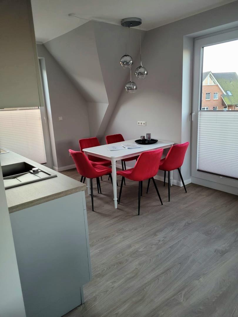 Essbereich mit weißem Tisch, roten Stühlen und Glaslampen. Holzboden und Fenster mit Jalousien.