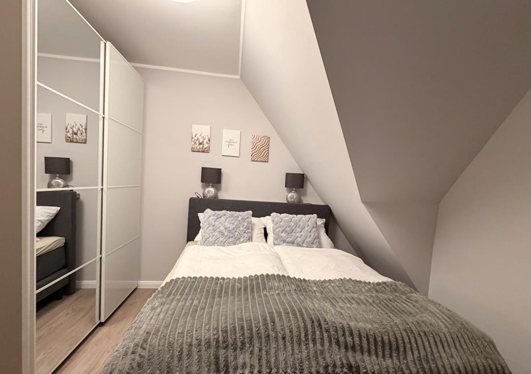 Schlafzimmer mit Dachschrägen, Bett, Nachttische und Spiegelschrank.