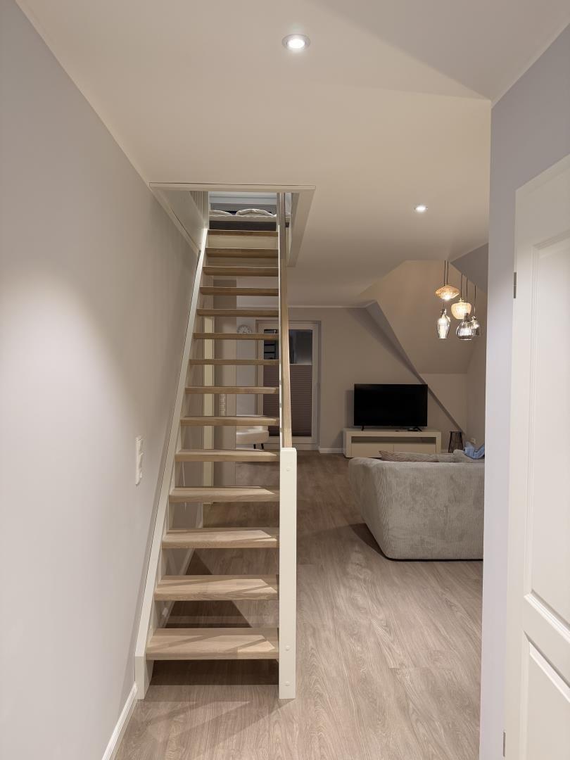 Treppenhaus führt zu Schlafzimmer. Wohnbereich mit Sofa und Fernseher.