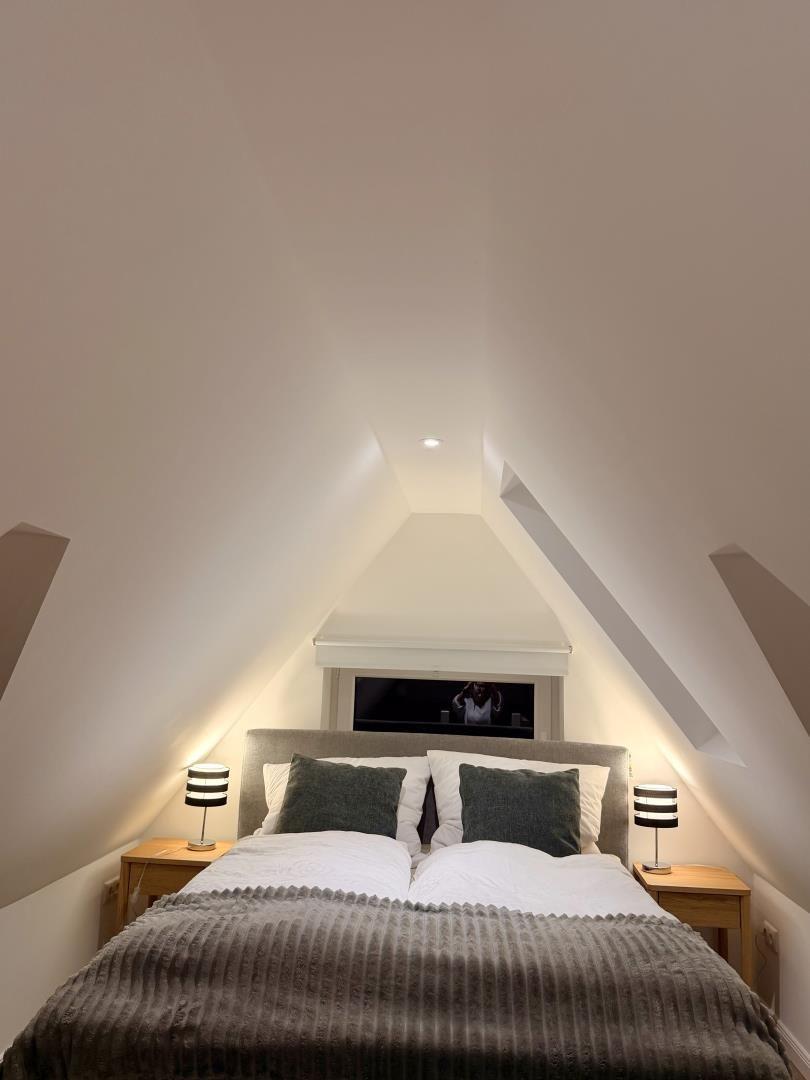 Schlafzimmer mit Doppelbett, zwei Nachttischen und schrägen Wänden.