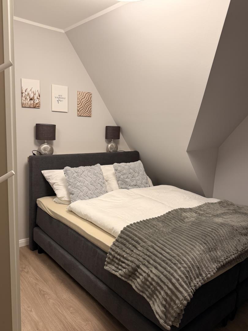 Schlafzimmer mit Doppelbett, zwei Nachttischen und drei Wandbildern.