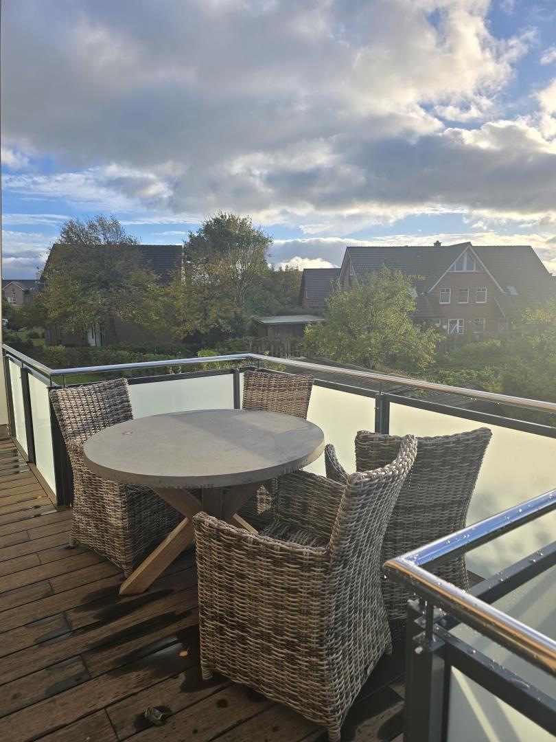 Terrasse mit Rattan-Tisch und Stühlen, Blick auf Wohnhäuser und Bäume.