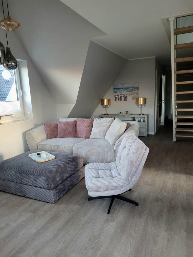 Wohnzimmer mit Sofa, Sessel und Holzboden unter Dachschrägen.