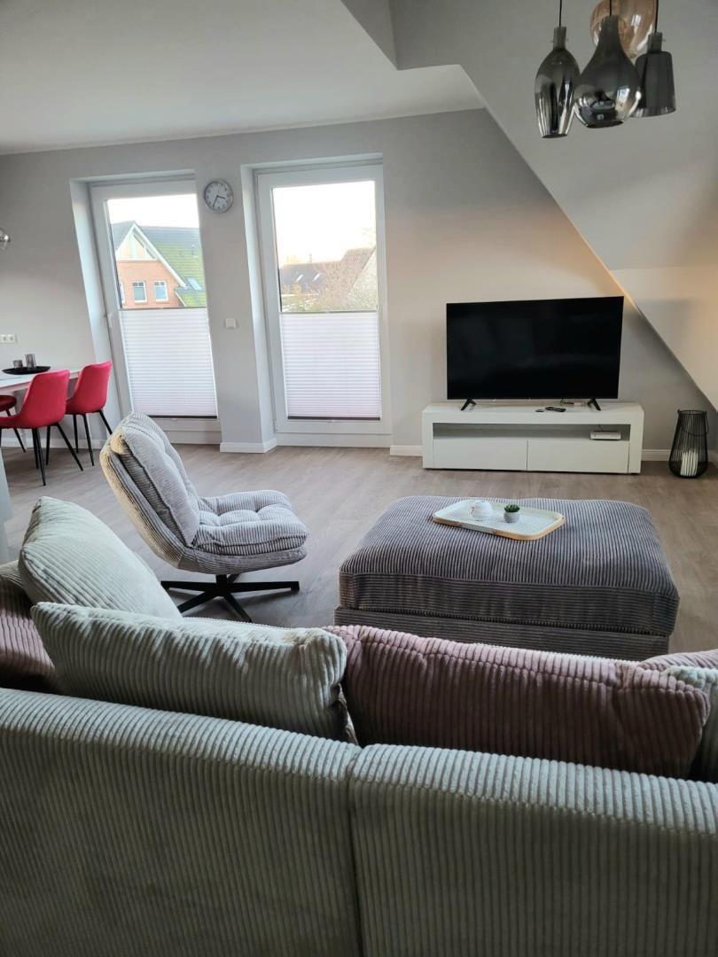 Wohnzimmer mit Sofa, Sessel, Fernseher und Fenstern.