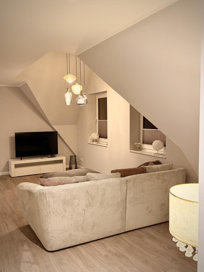 Wohnzimmer mit Sofa, Fernseher und schrägen Wänden.