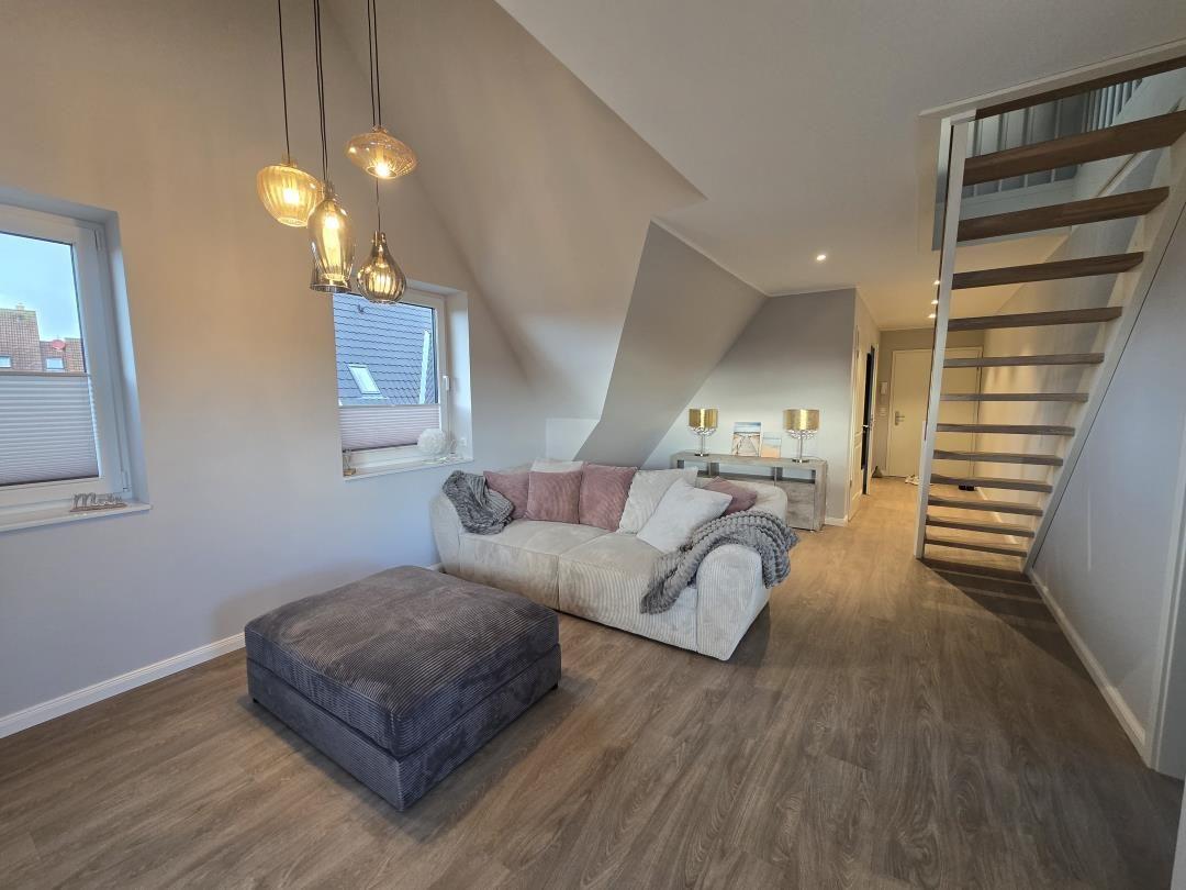 Wohnzimmer mit Sofa, Hocker und Treppe zur oberen Etage.
