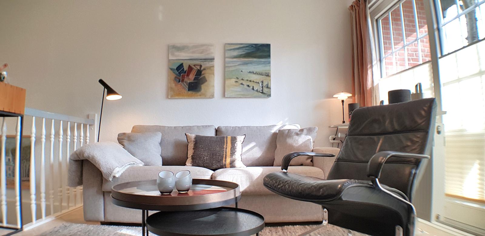 Wohnzimmer mit Sofa, Sessel und Tisch. An der Wand hängen zwei Bilder.