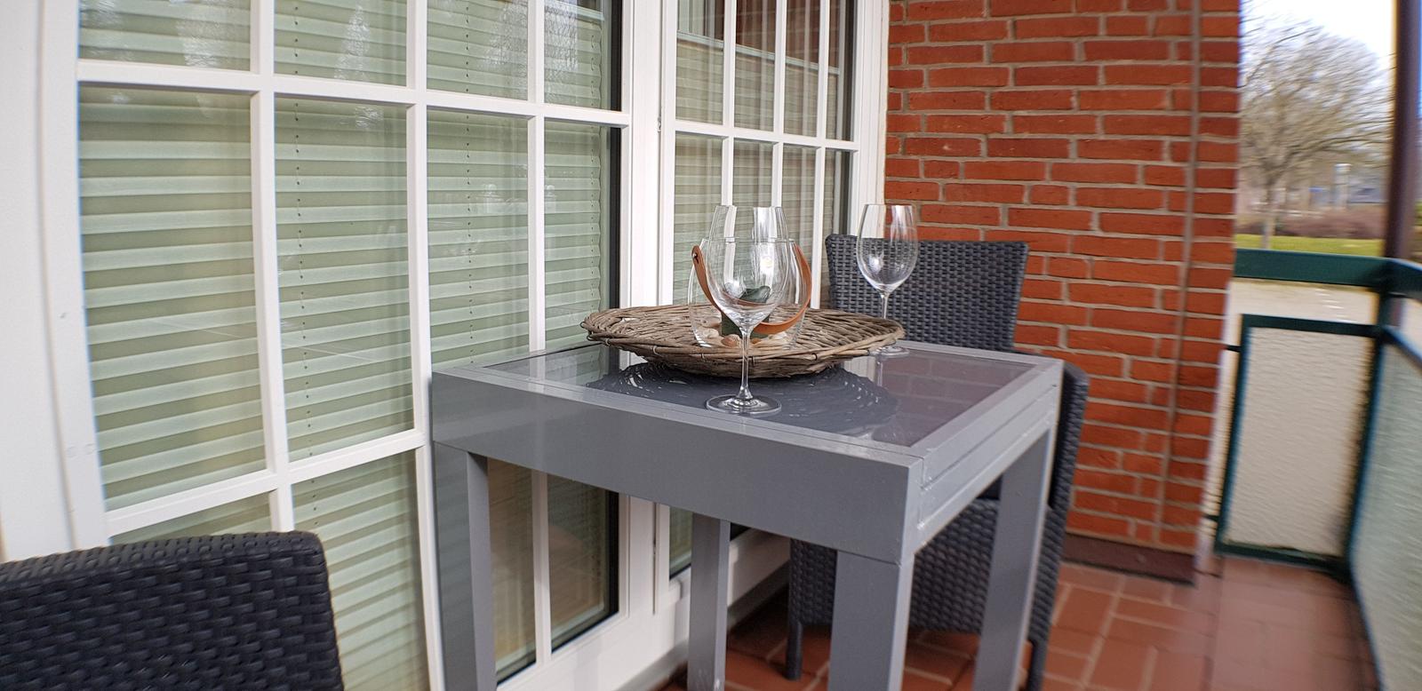 Terrasse mit Tisch, Stühlen und Weingläsern vor Fenster und Backsteinwand.