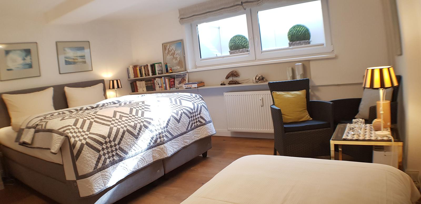 Schlafzimmer mit Bett, Sessel und Fenster mit Pflanzen.