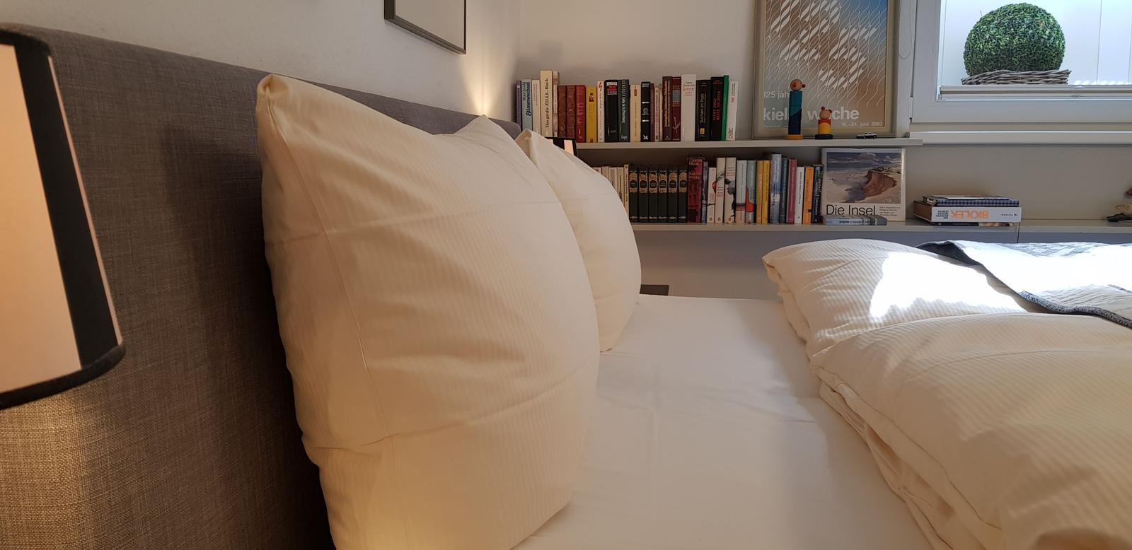 Schlafzimmer mit Bett, Kissen und Bücherregal an der Wand.