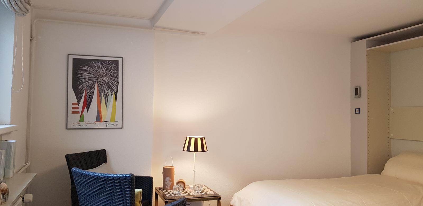 Schlafzimmer mit Bett, Nachttisch, Lampe und Wandbild.