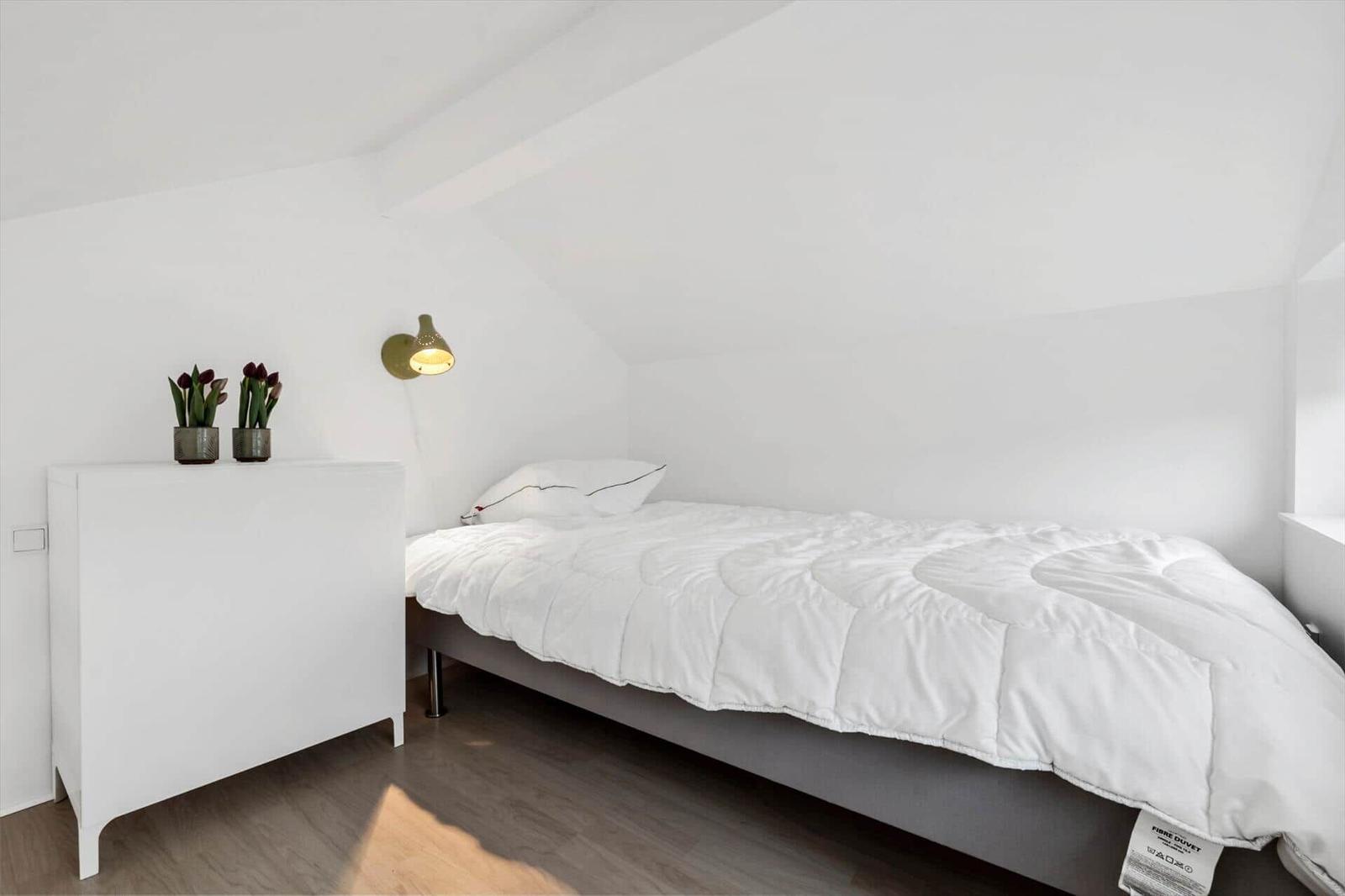 Bedroom with bed, nightstand, and wall lamp under sloped ceiling.