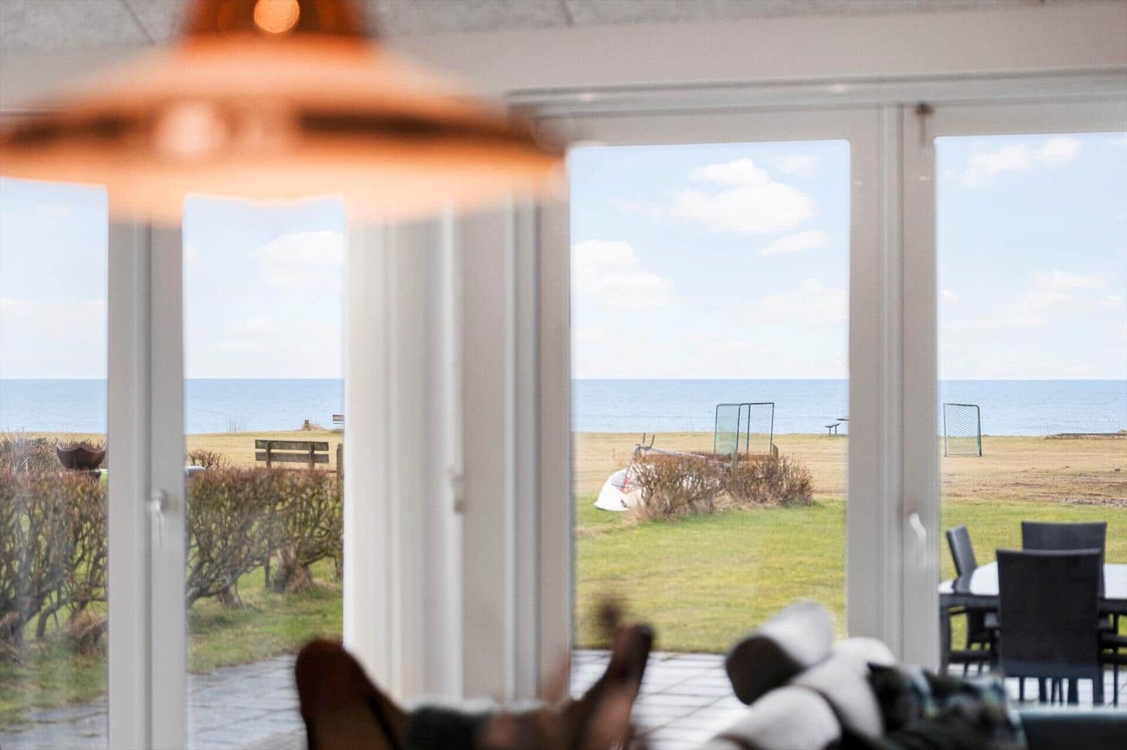 Large windows offer view of sea and lawn with outdoor table and chairs.