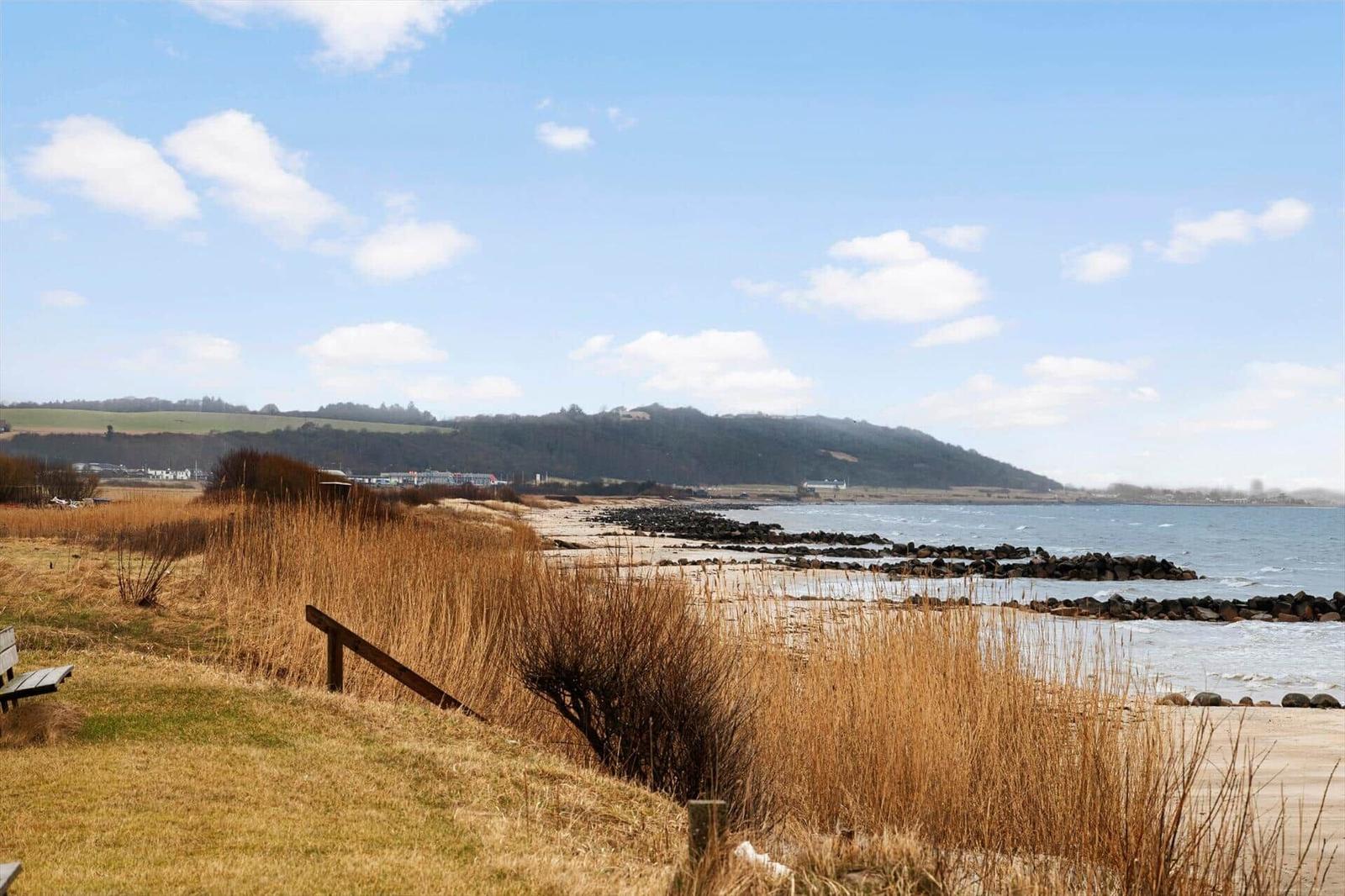 Beach with rock protection, dry grass, and hillside landscape in the background.