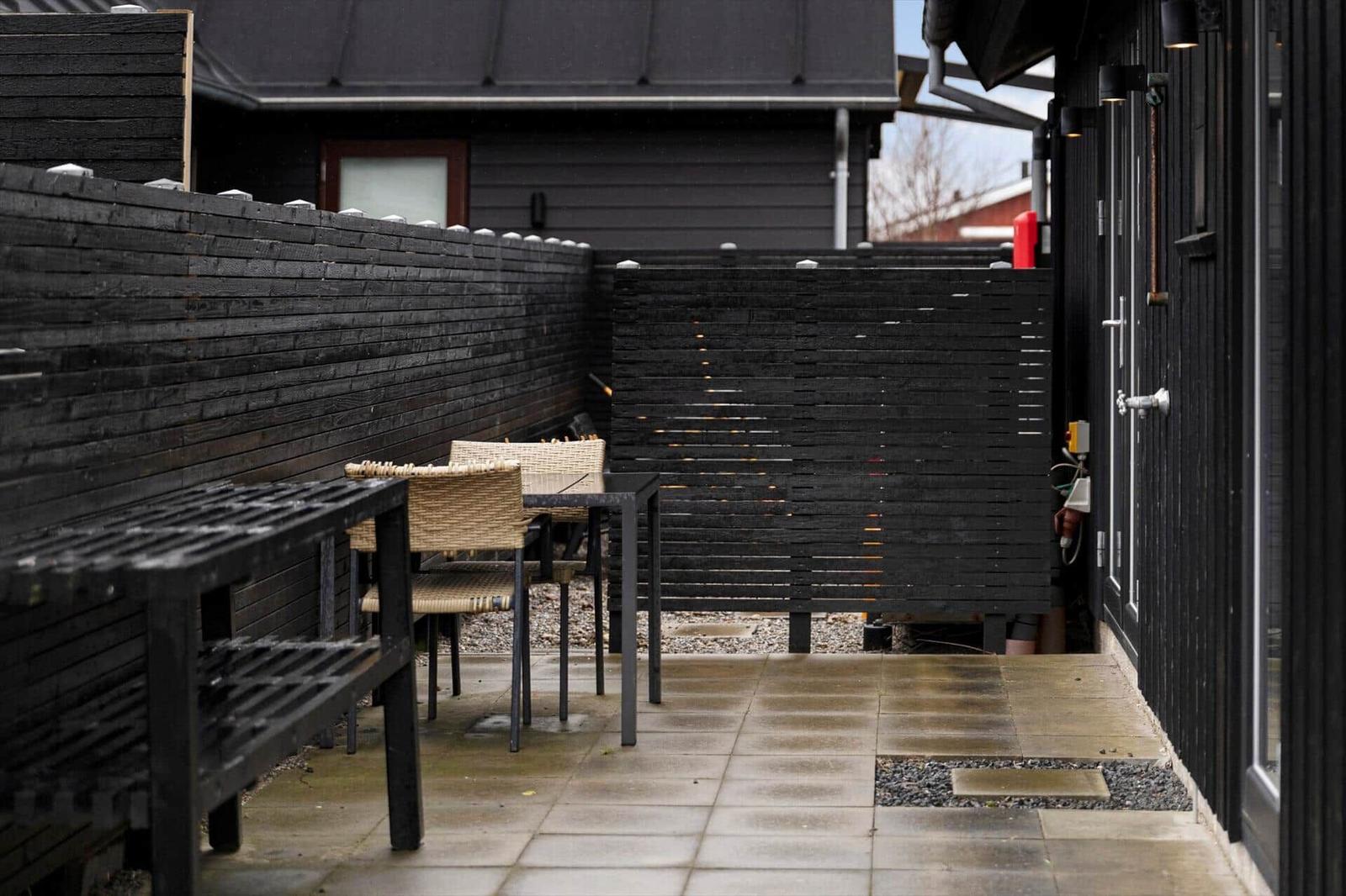 Terrace with table, chairs, and dark wooden walls. Tile floor and slatted fence visible.