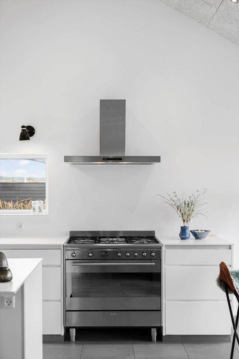 Modern kitchen with stainless steel stove and range hood. White countertops and window.