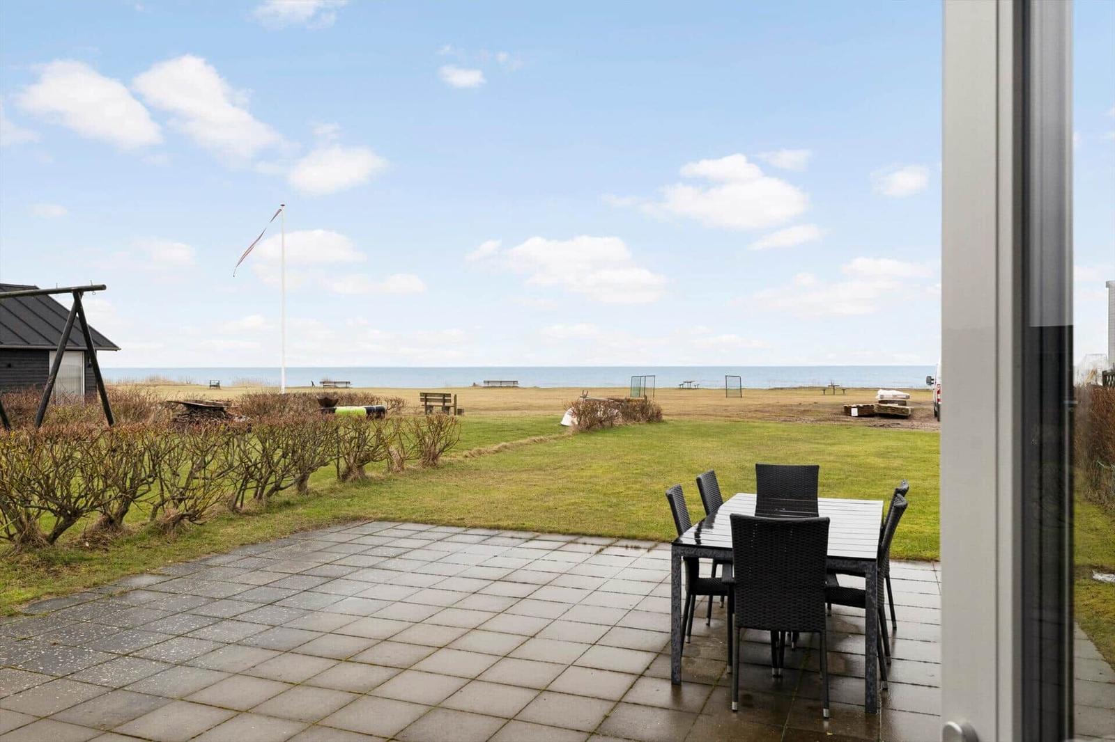 Terrace with table and chairs, view of beach and sea.