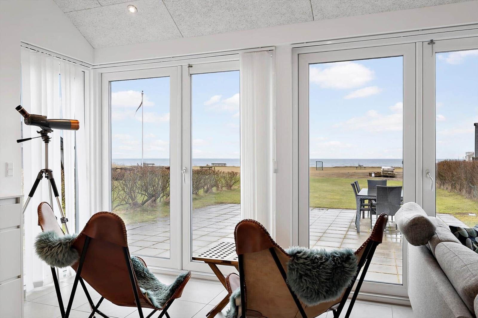 Living room with view of beach and terrace with garden furniture and telescope.